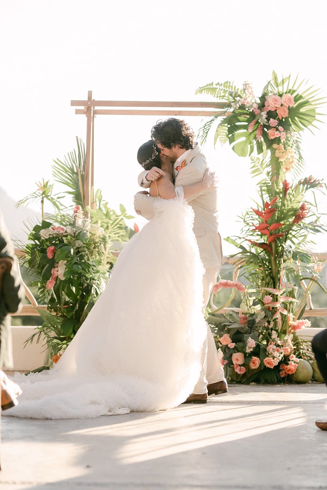 Los novios se abrazan frente al altar de flores tropicales