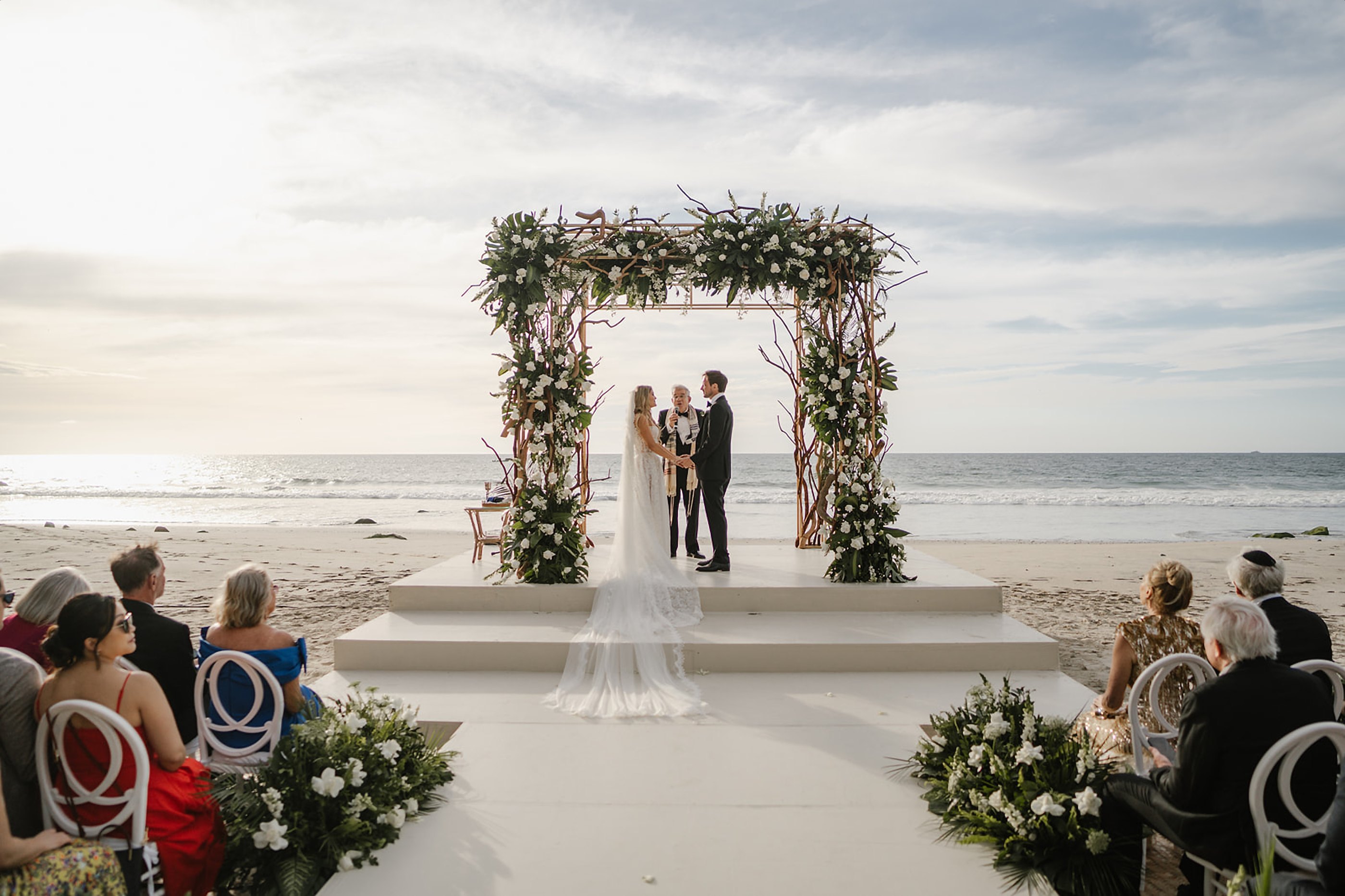 Ceremonia en la playa bajo un altar de flores blancas, frente al Pacífico