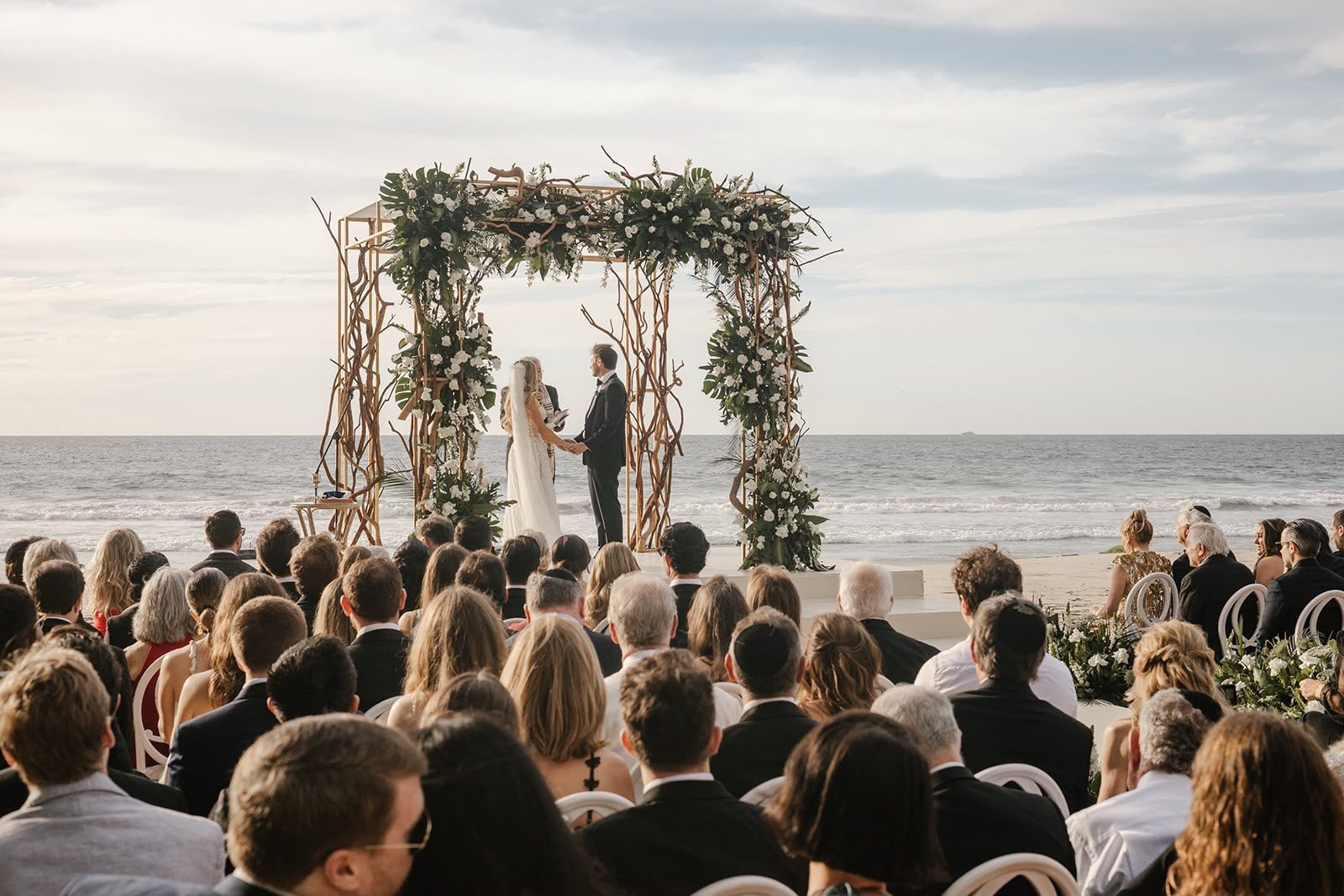 Los invitados durante la ceremonia, con la jupá y el mar de fondo