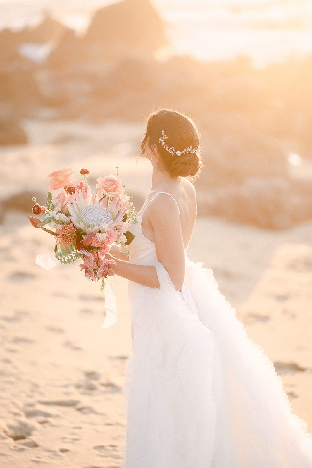 La novia con su ramo, de espaldas, con la luz del atardecer sobre la arena